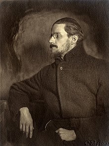 Half-length portrait of man in his thirties. He looks to his right so that his face is in profile. He has a mustache, a thin beard, and medium-length hair slicked back, and wears a pince-nez and a plain dark greatcoat, looking vaguely like a Russian revolutionary. Half-length portrait of man in his thirties. He looks to his right so that his face is in profile. He has a mustache, a thin beard, and medium-length hair slicked back, and wears a pince-nez and a plain dark greatcoat, looking vaguely like a Russian revolutionary.